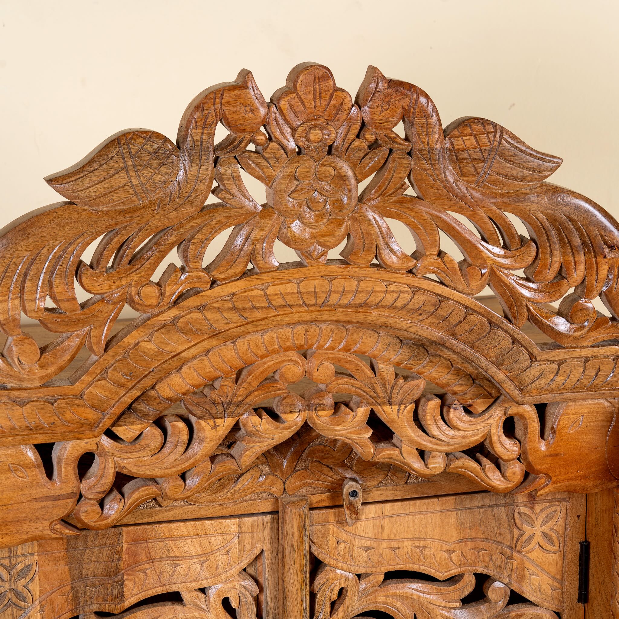 Close up image of a hand carved mango wood Indian mandir temple with ornate floral carvings, lattice doors, and two storage drawers.