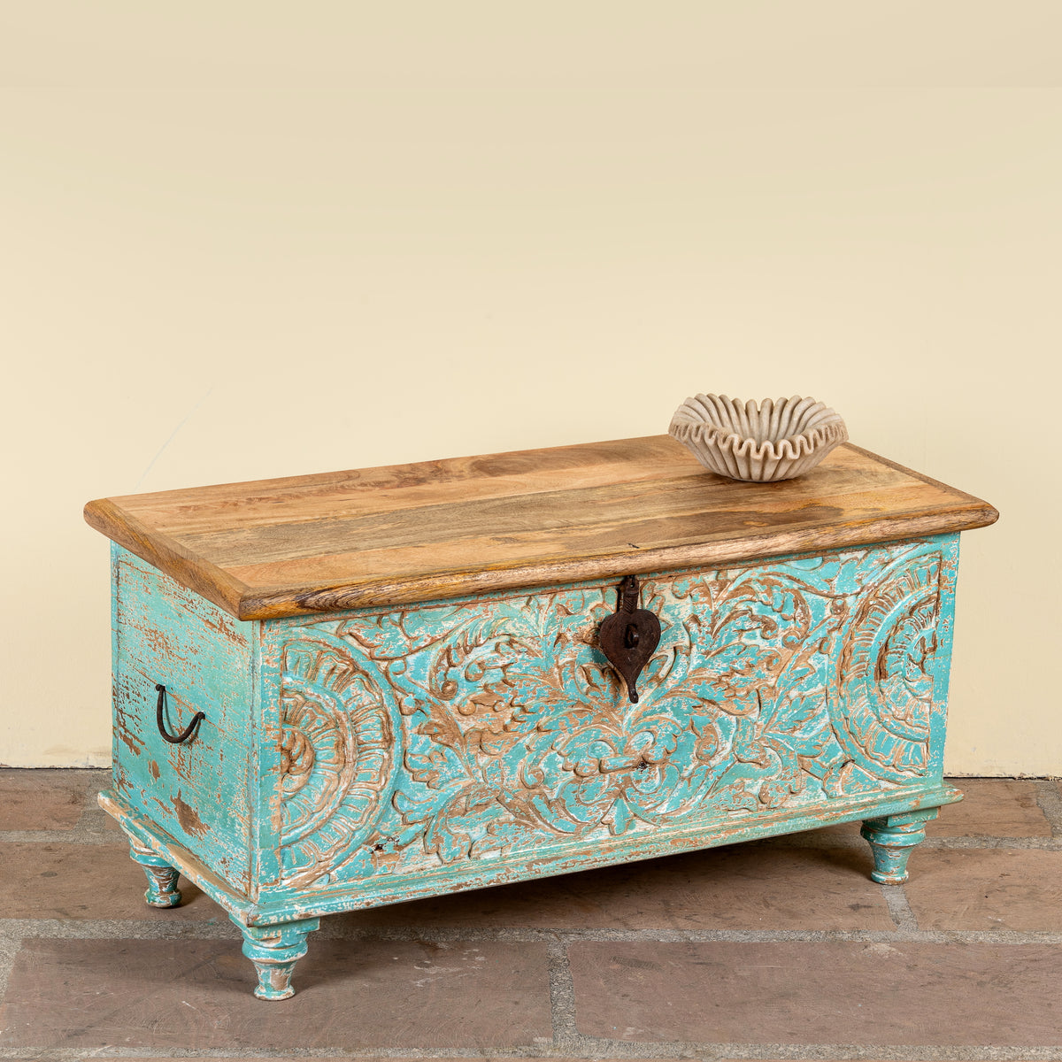 Side angle image of a Neysa hand carved mango wood chest coffee table with turquoise floral design, natural wood top and iron lock, 90cm wide