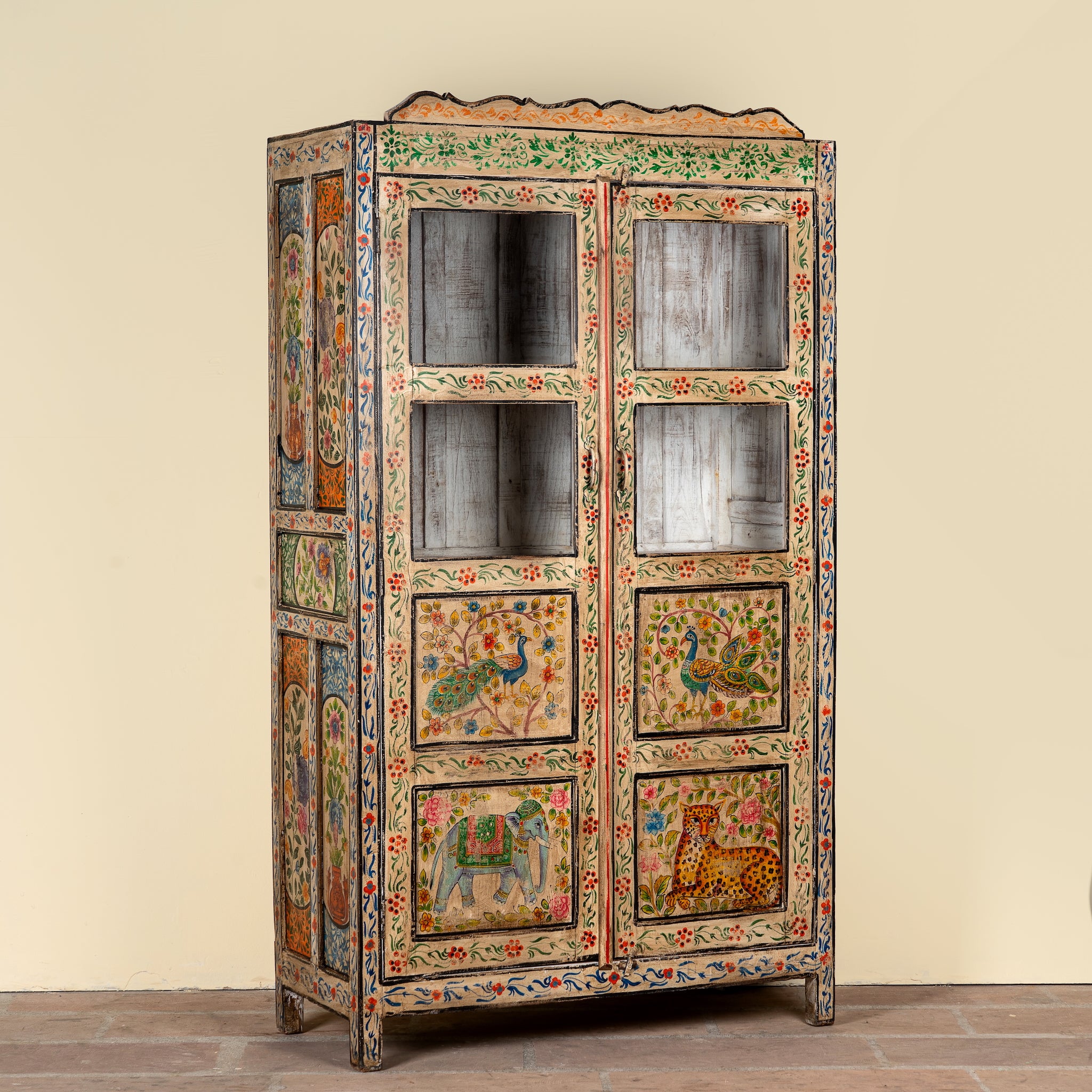 Side angle image of a Nirav hand painted reclaimed teak display cabinet with floral, peacock, elephant and leopard motifs 190cm