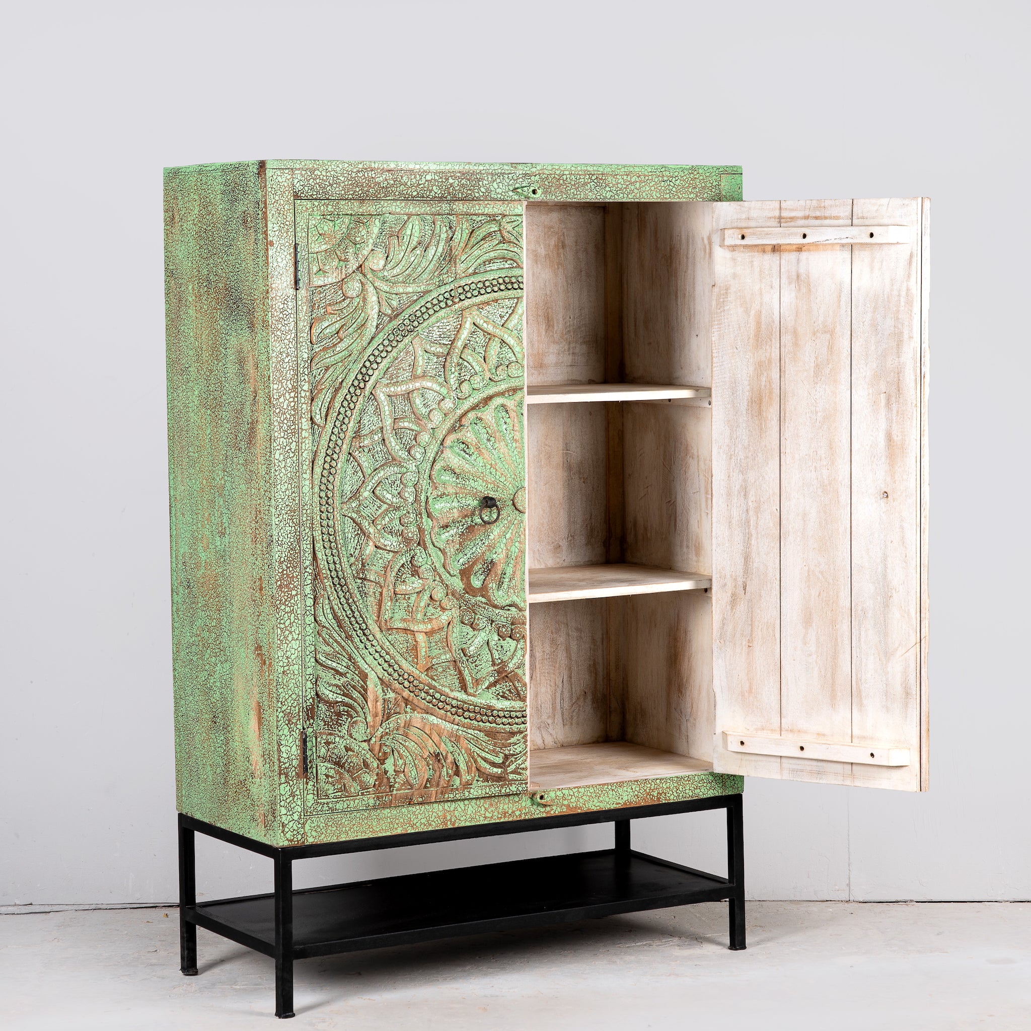 Image showing open door of a carved mango wood cabinet with floral hand-carving, distressed green finish, iron stand, 100 × 40 × 150 cm.