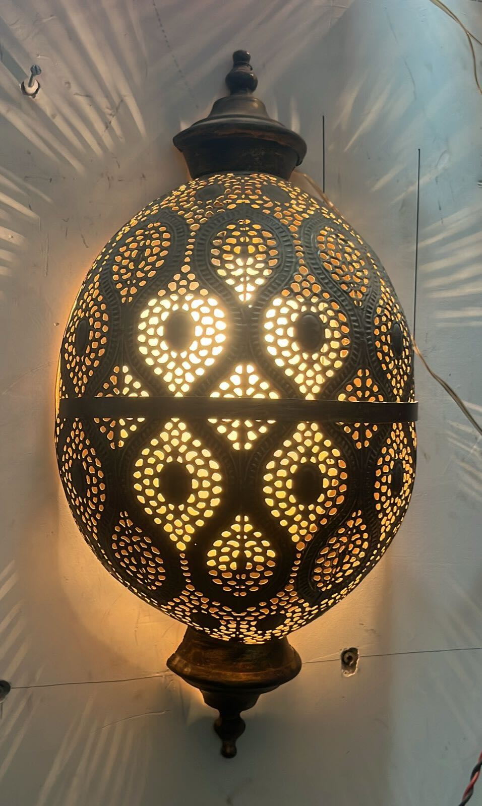 Close up image of a antique-style hand-stamped iron wall lamp with brass finish, featuring intricate perforated detailing and vintage ornamental shape.