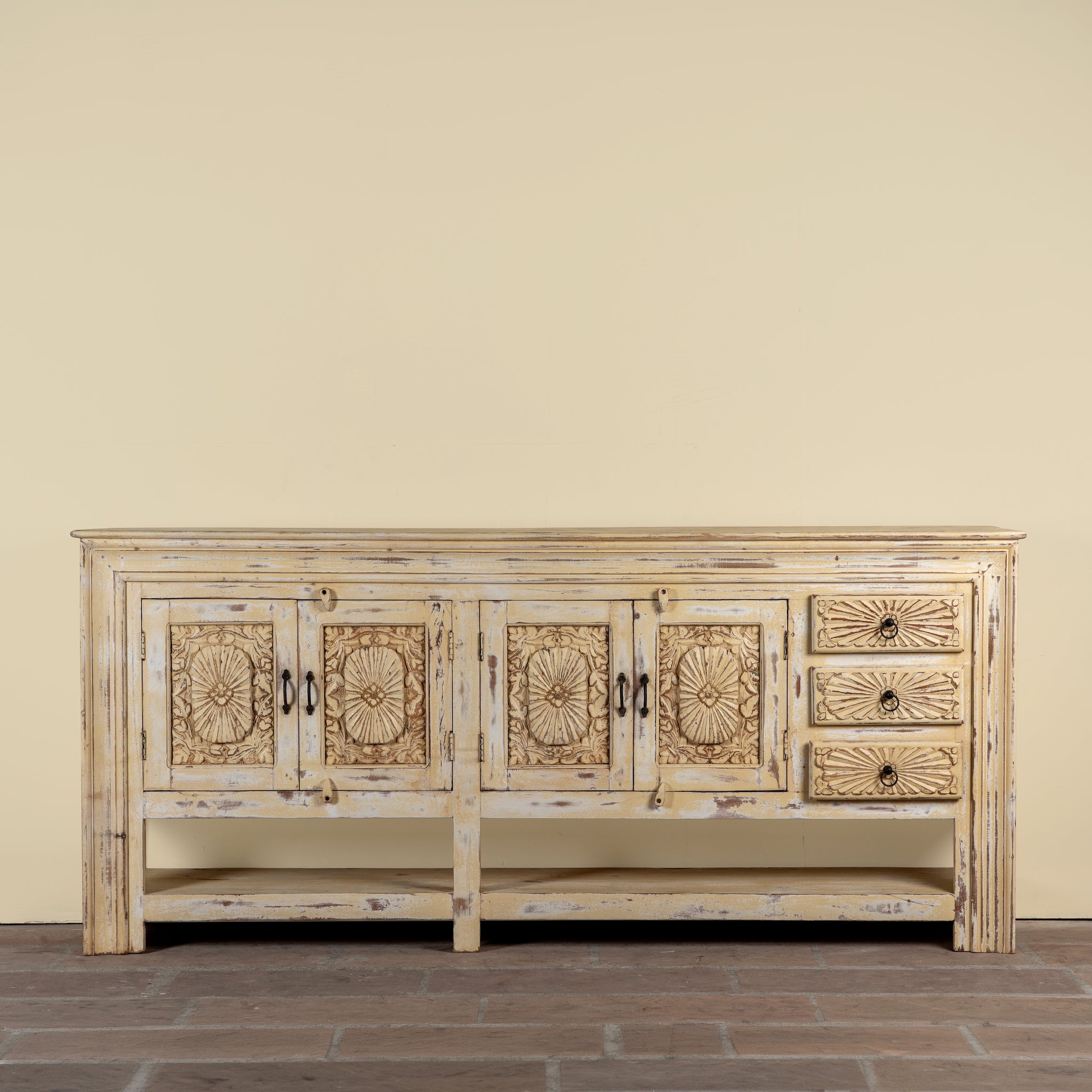 Ranjit reclaimed wood vintage console table with cream distressed finish, carved doors, three drawers and open lower shelf.