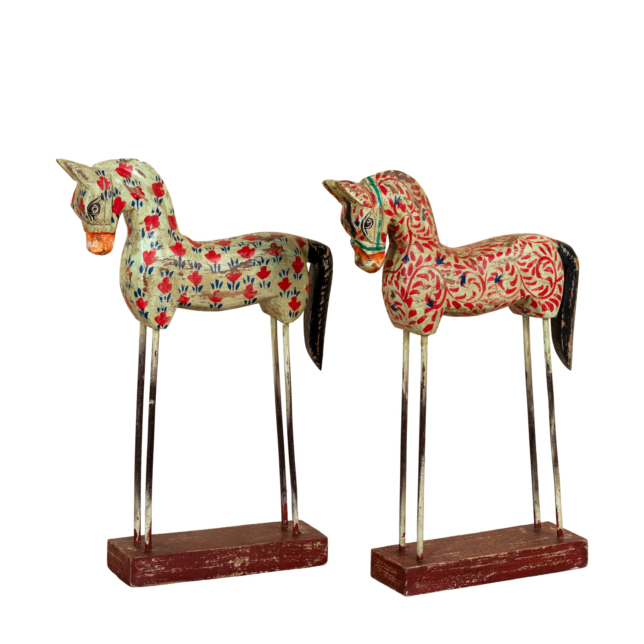 A pair of traditional Indian wooden horse statues with intricate floral patterns, mounted on metal wire legs and painted reddish-brown bases, set against a plain white background.