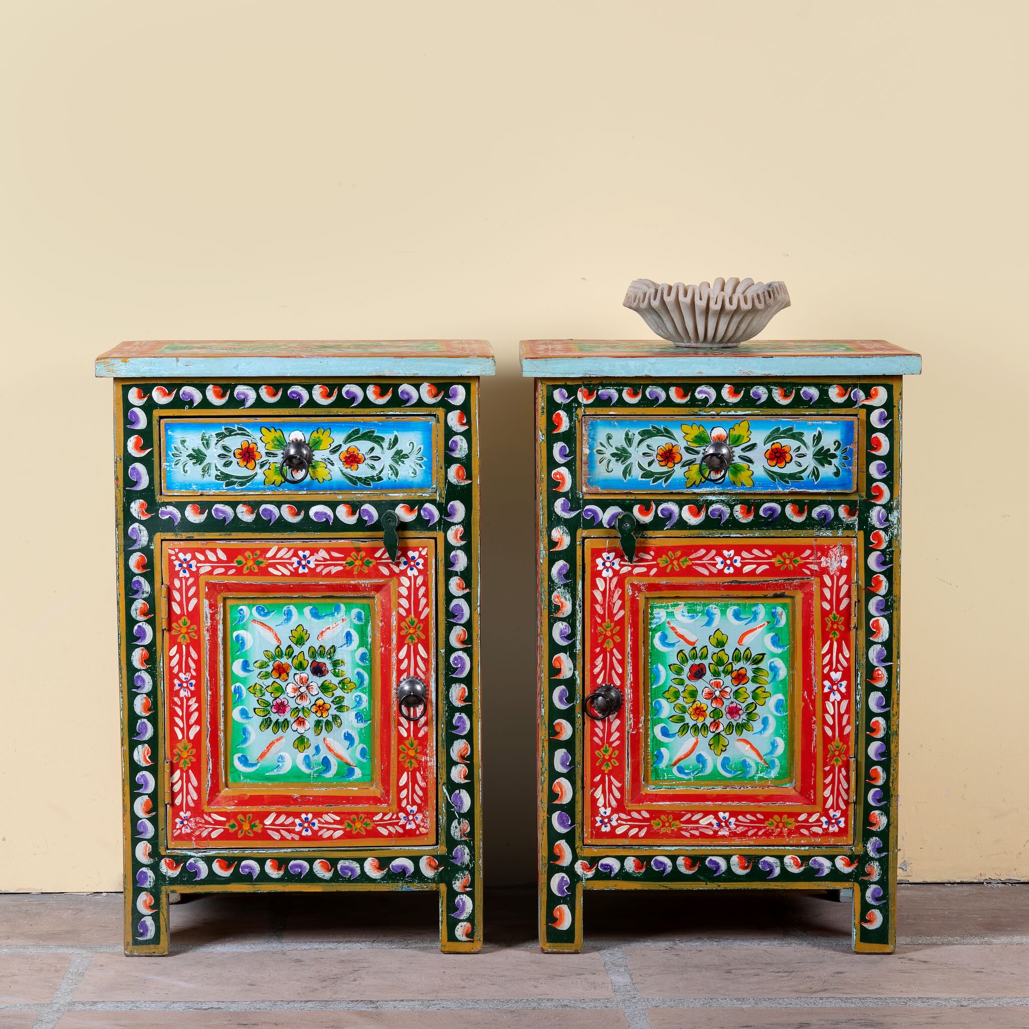 Image of a pair of hand-painted bedside tables made from recycled wood – vintage night stands with carved mango wood furniture detailing and floral artistry.