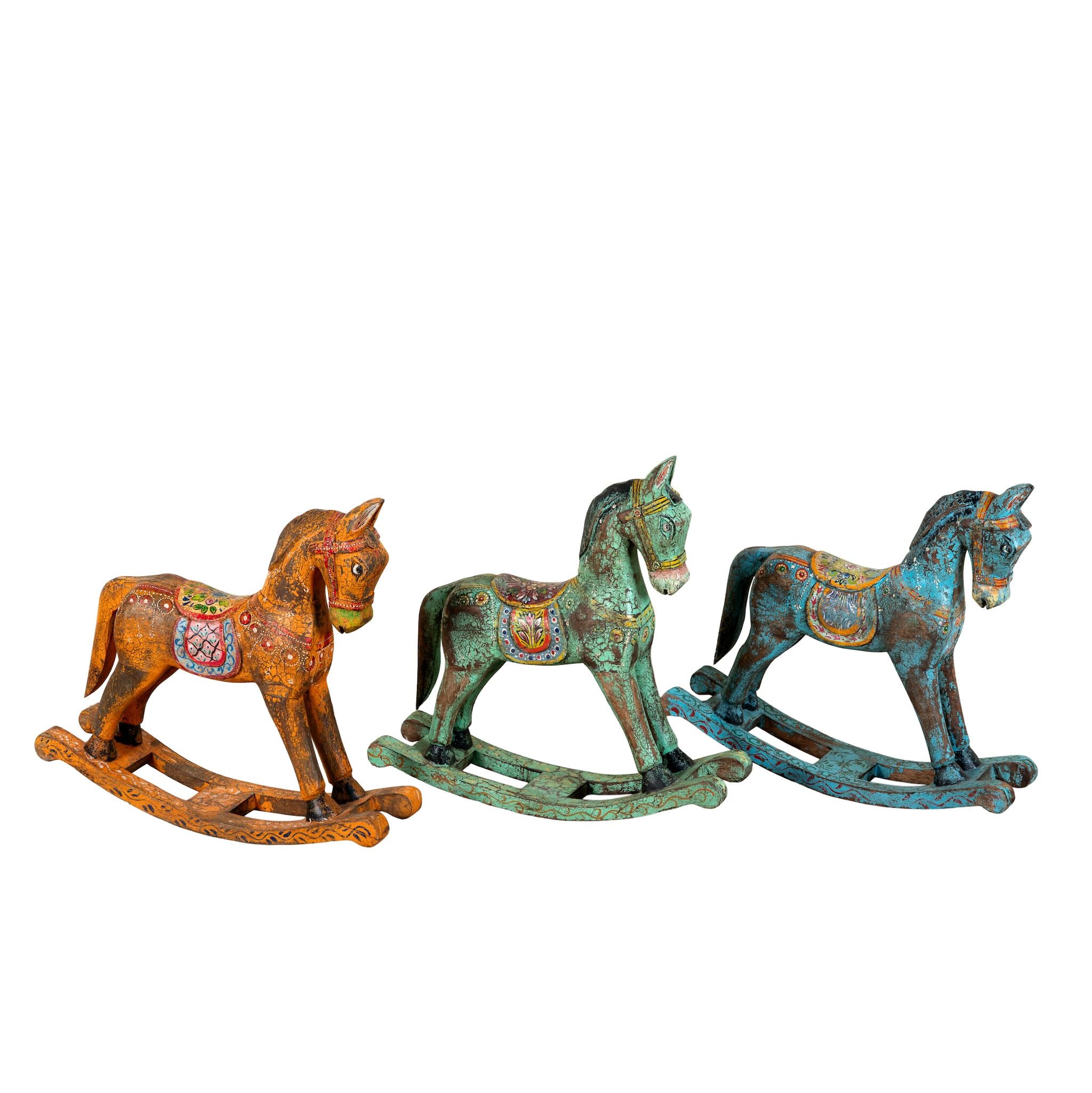 White background image of a colourful hand-painted wooden rocking horses with ornate saddle patterns, crafted in India. Unique bohemian interior décor accents made from solid wood, perfect for shelves or sideboards.
