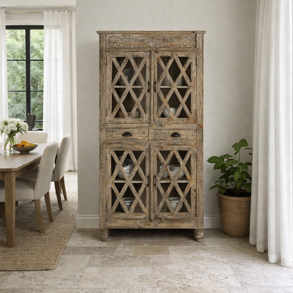 Lifestyle image of a of a vintage display cabinet made from solid mango wood with glass doors and shelving – handcrafted Ibiza-style showcase with carved details.