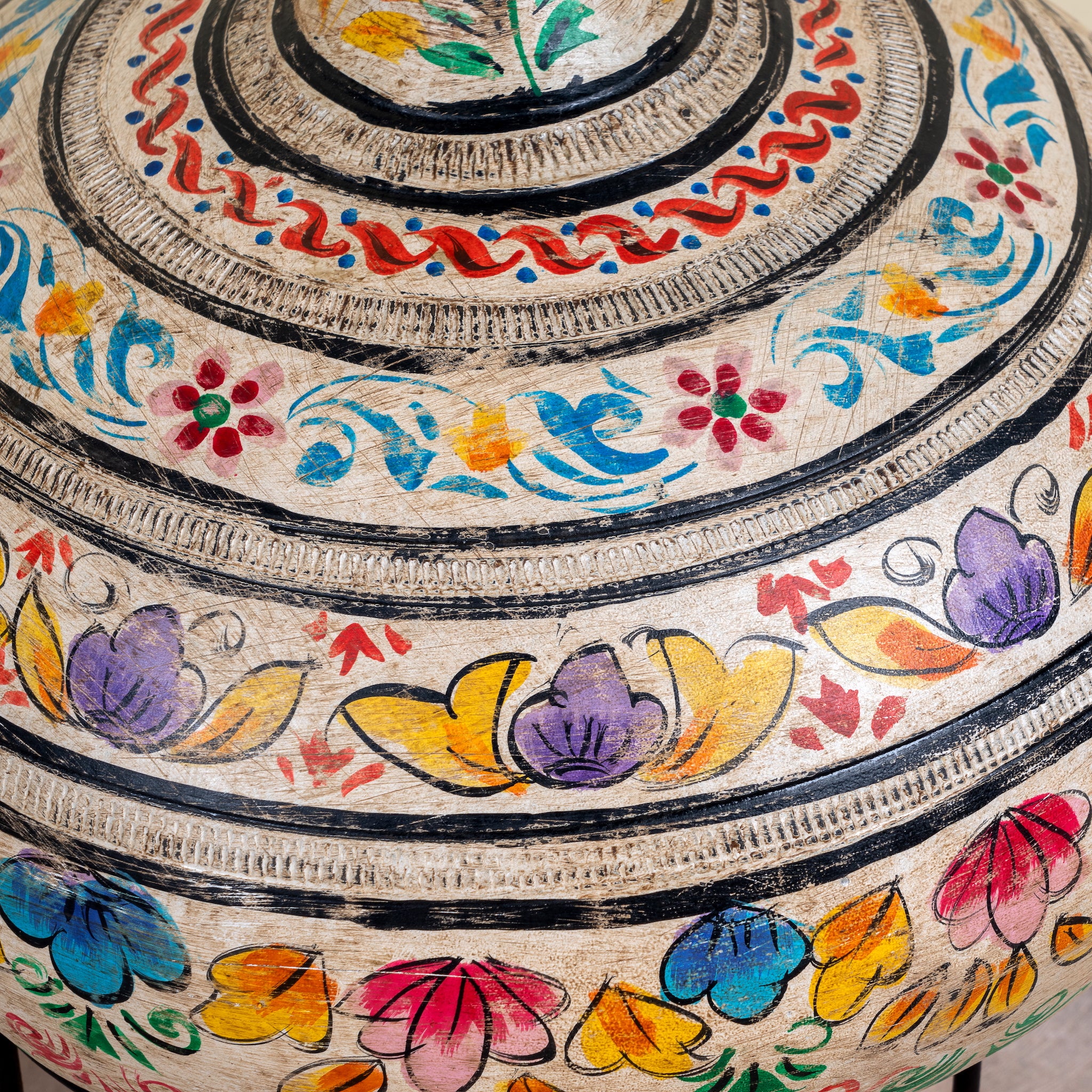 Close up image of a hand-painted clay vase with colourful floral motifs, rounded body, narrow neck and iron stand, handcrafted decorative vase, 40cm.