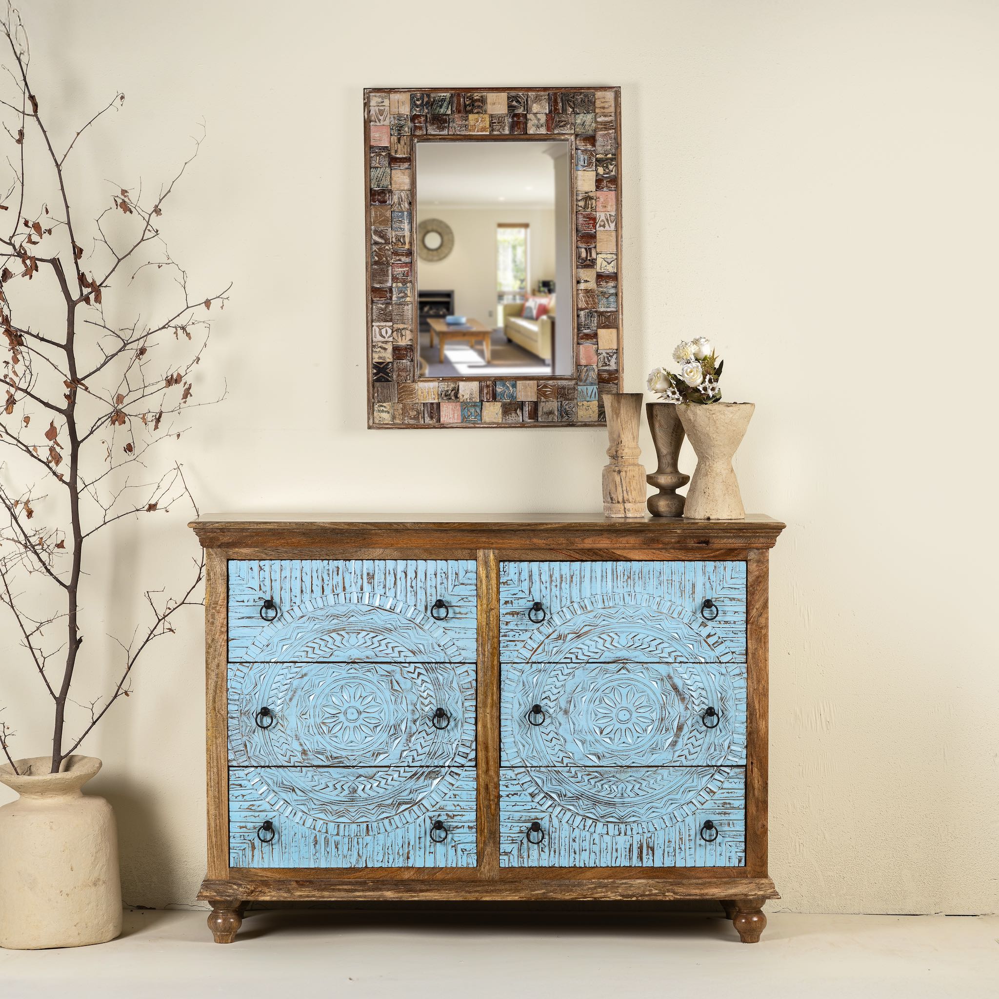 Lifestyle image of a hand-carved mango wood chest of drawers Safita with distressed blue finish and iron fittings, boho style living room furniture, 140 × 42 × 100 cm.