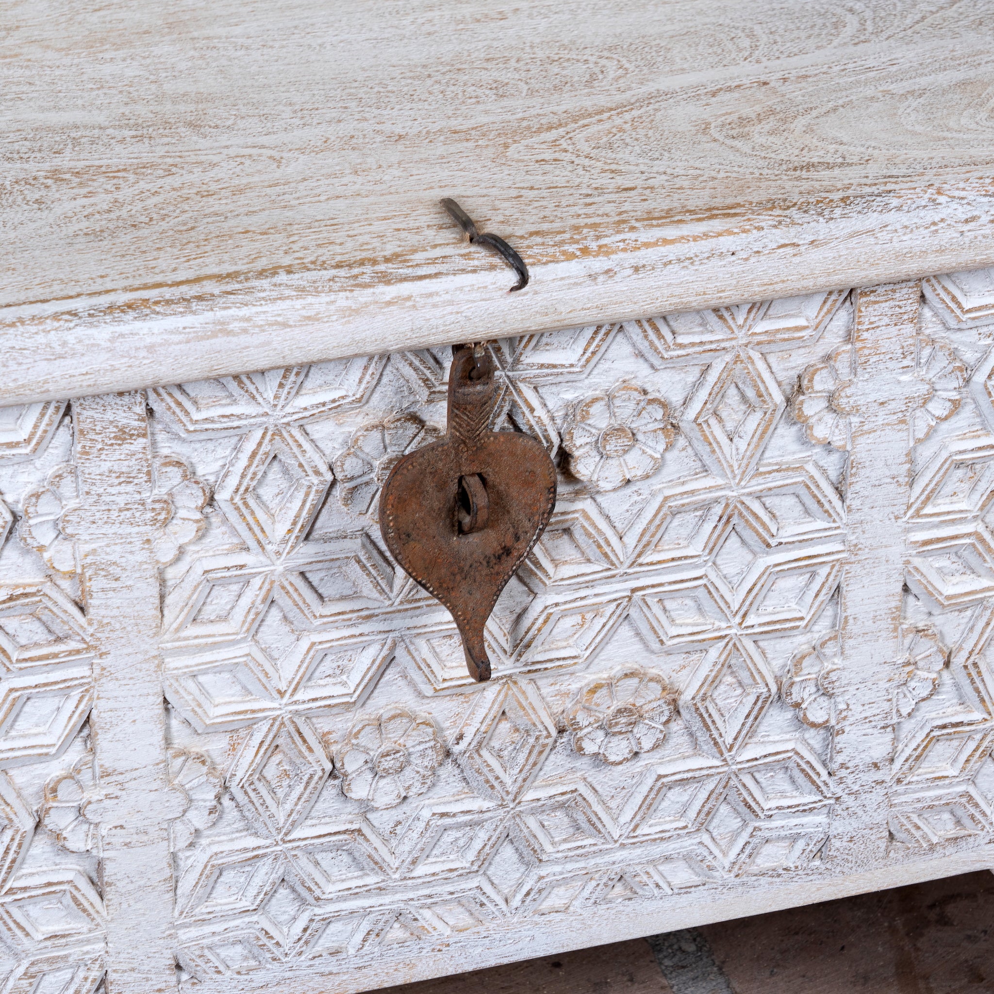 Close up image of a Samay mango wood storage chest coffee table with carved geometric front, iron fittings, wooden wheels and distressed finish 120cm