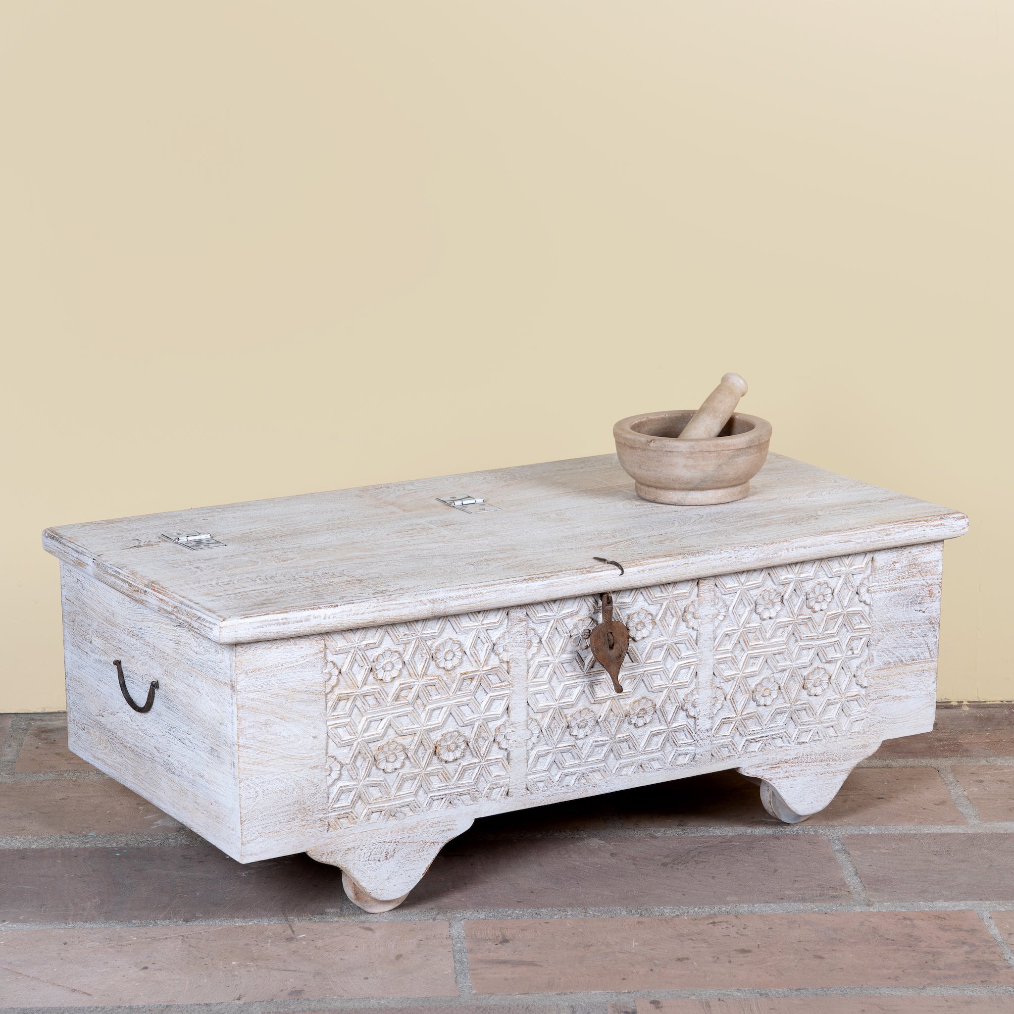 Side angle image of a Samay mango wood storage chest coffee table with carved geometric front, iron fittings, wooden wheels and distressed finish 120cm