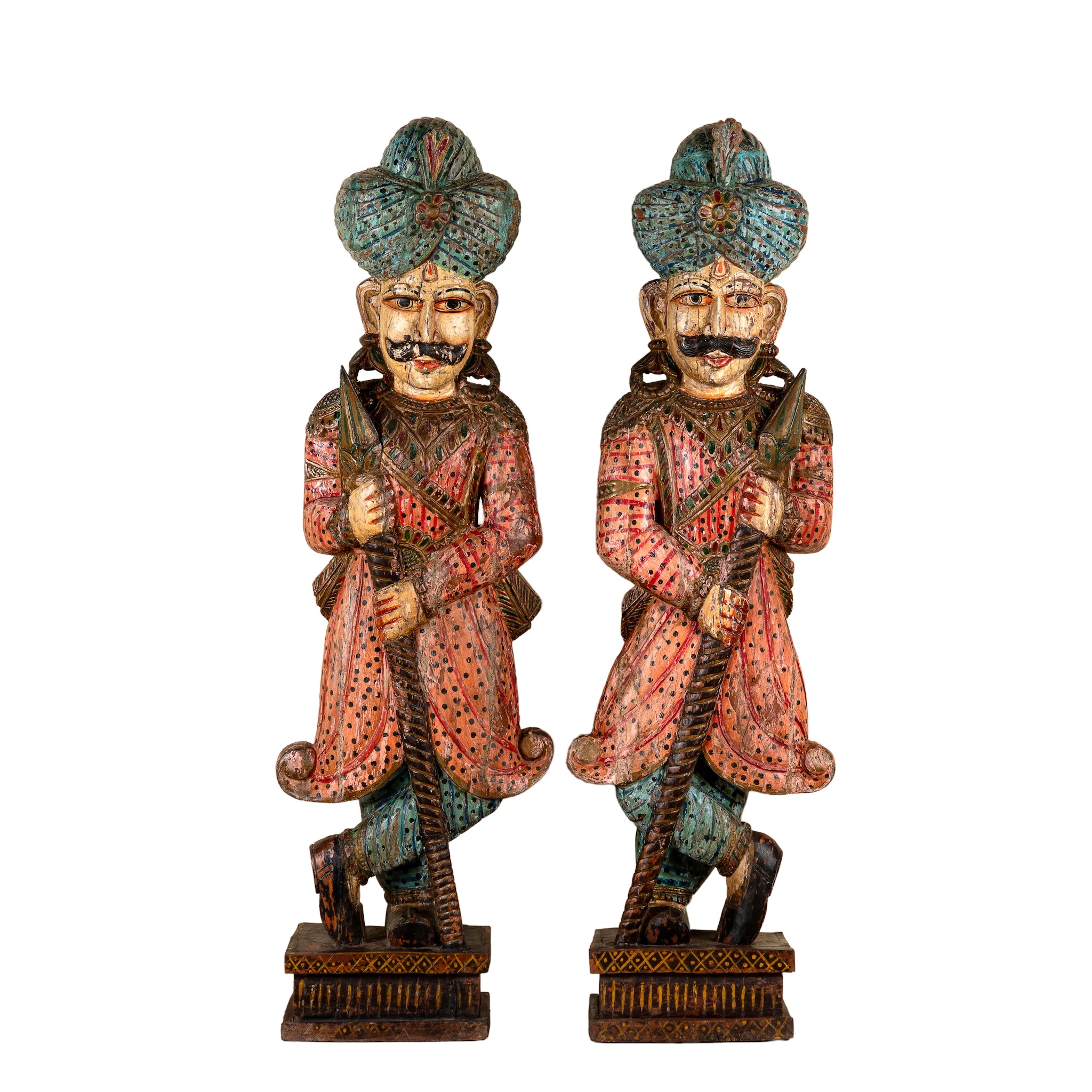 A pair of hand-carved wooden figurines of Indian Rajasthani nobles wearing turquoise and red patterned garments, standing on ornate bases against a white background.