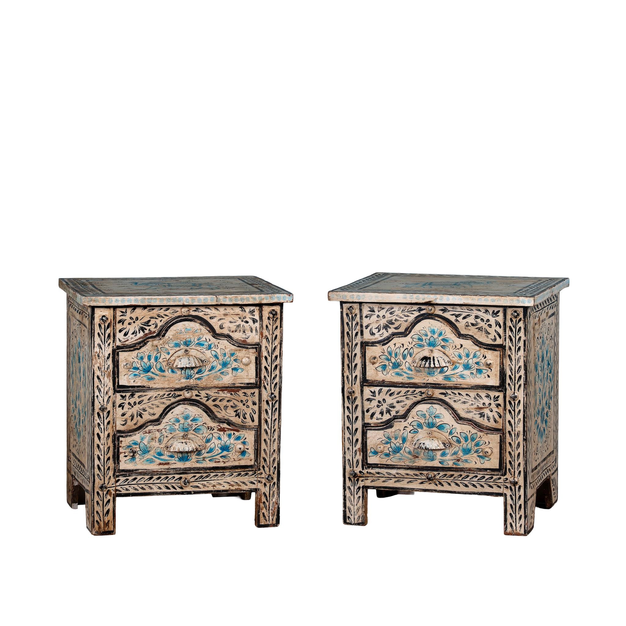 White background picture of a pair of hand-painted nightstands made from reclaimed wood, featuring floral motifs in soft turquoise and black with intricate carved detailing and two drawers for storage.