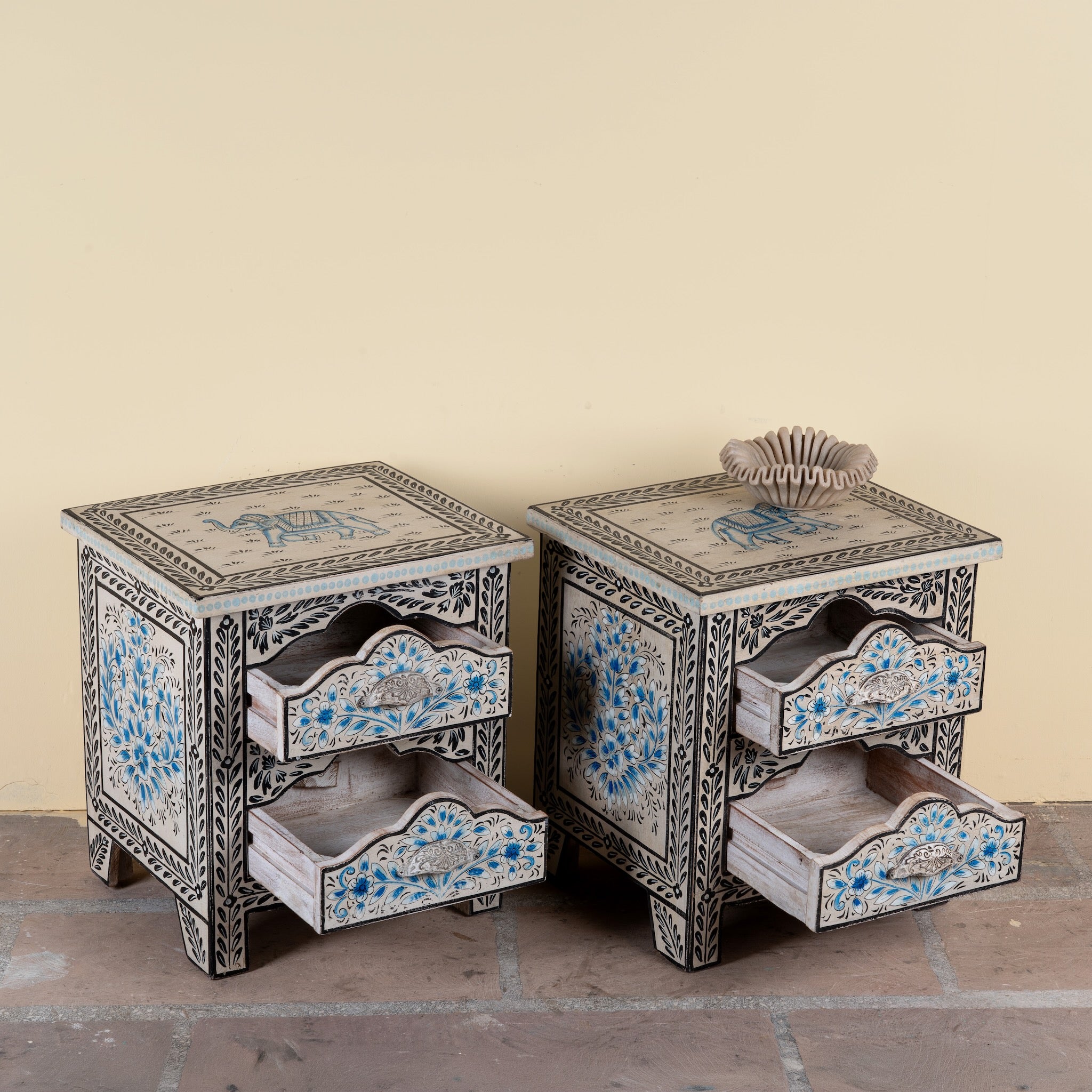 Side angle image with open drawers of a pair of hand-painted nightstands made from reclaimed wood, featuring floral motifs in soft turquoise and black with intricate carved detailing and two drawers for storage.