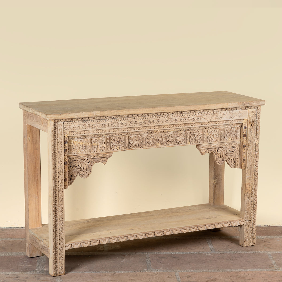 Side angle image of a Shivam hand carved reclaimed teak wood console table with decorative old Indian house elements and open storage shelf, 132cm wide