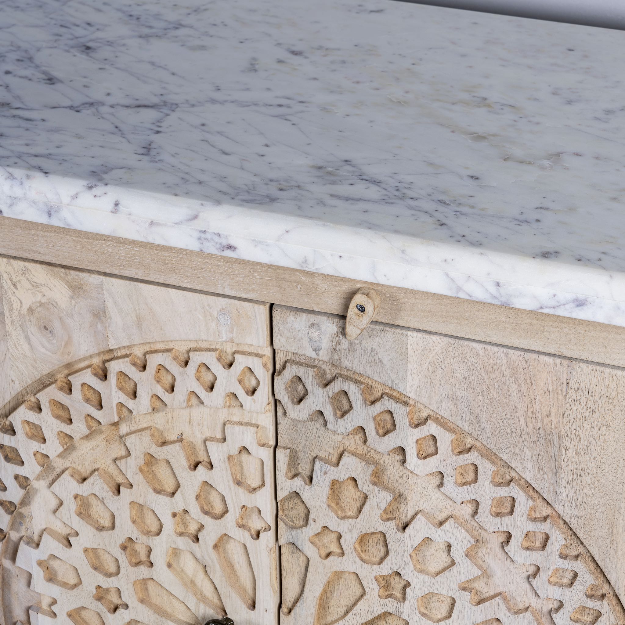 Close up picture of a Acacia wood sideboard with circular carvings, 4 doors and iron handles with a white marble top.