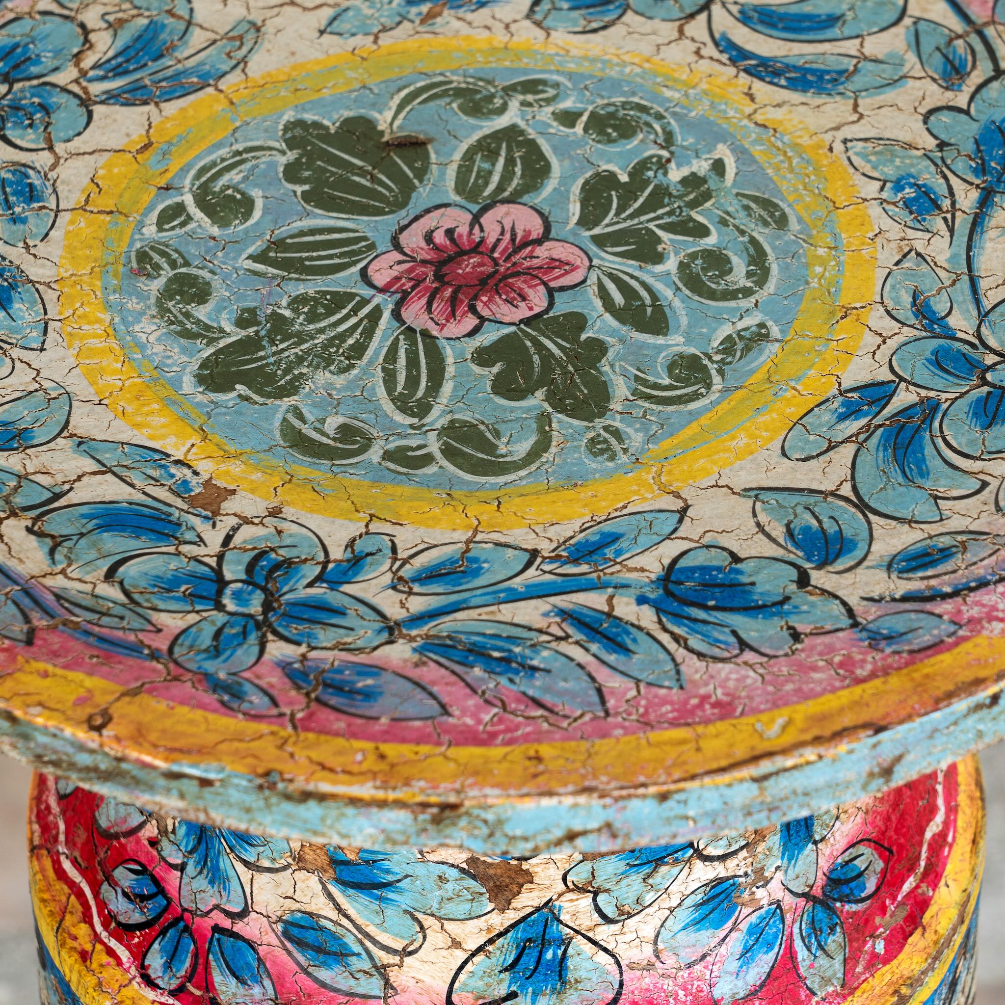 Close up image of a hand‑painted wooden side table with floral motifs in vibrant colours, perfect for bohemian interiors and artisanal furniture displays.