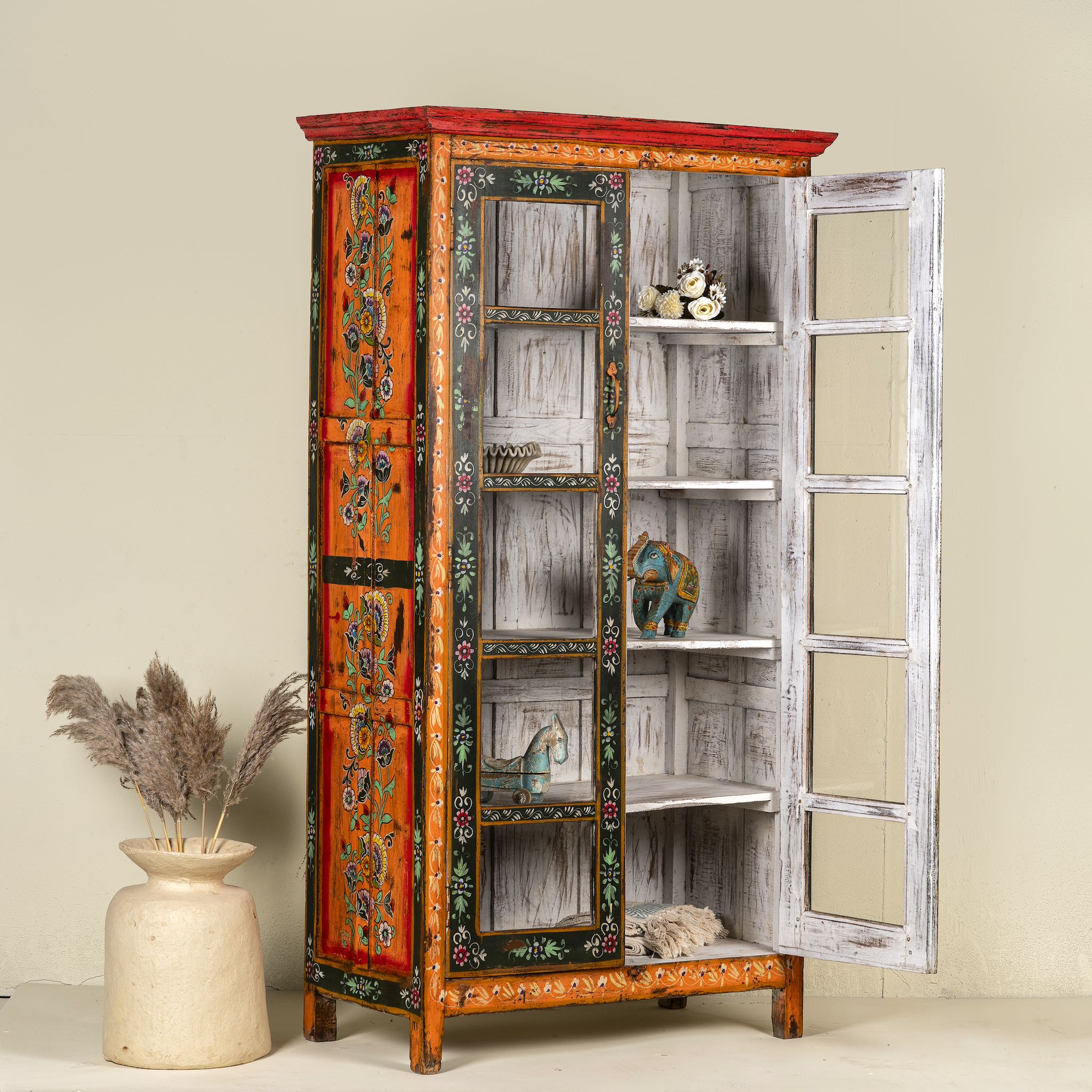 Side angle image with open doors of a hand-painted reclaimed wood showcase with floral motifs and glass doors – sustainable furniture combining vintage charm and traditional craftsmanship.