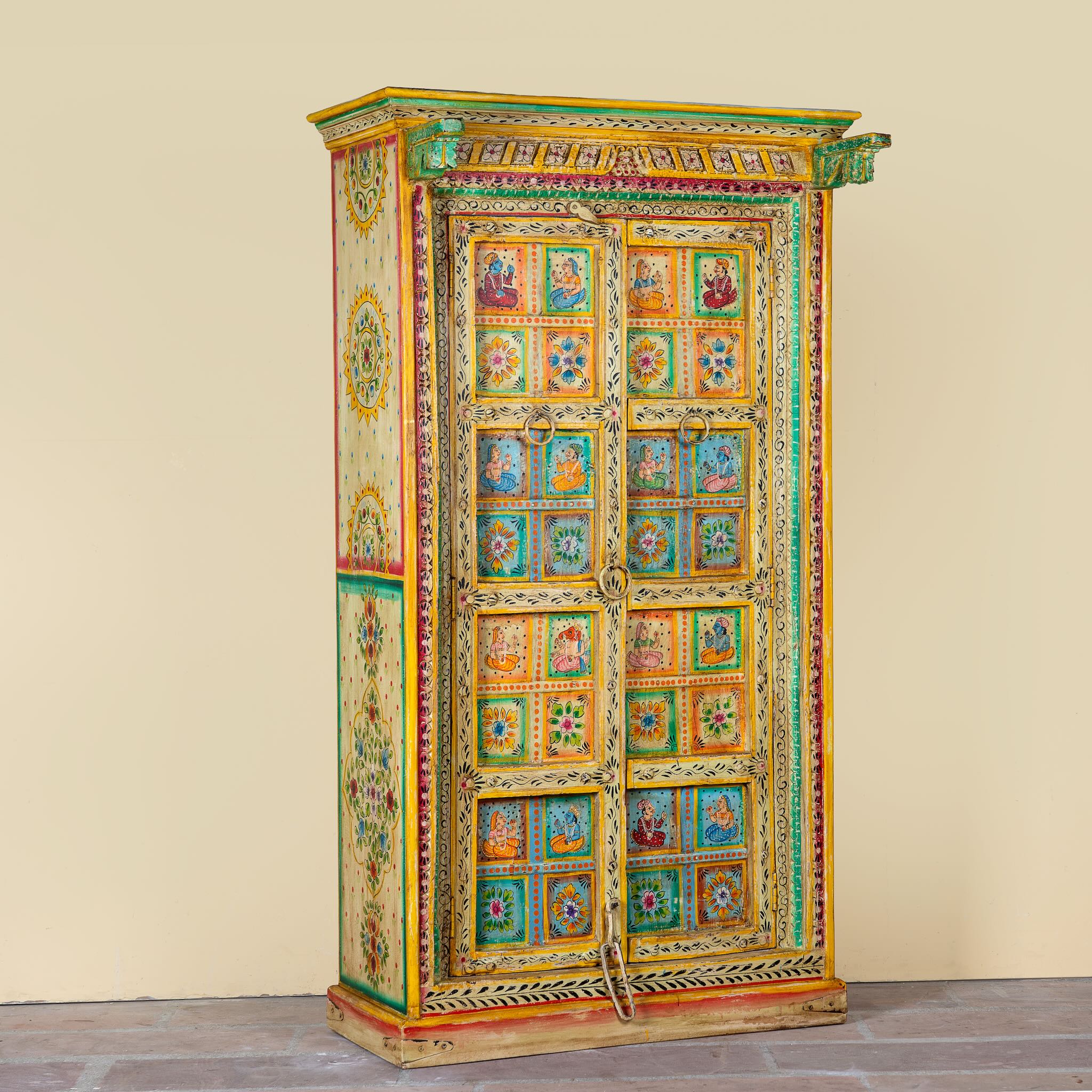 Side angle image of a hand painted wardrobe made of teak wood with floral motifs; unique furniture inspired by Indian artistry, 104 × 50 × 186 cm.