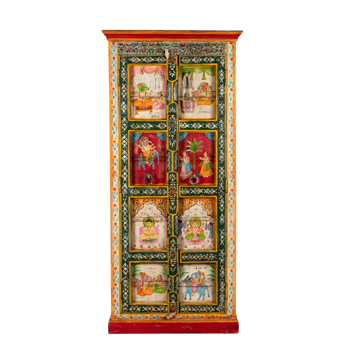 White background image of a a tall, hand-painted Indian wooden cabinet with colorful traditional illustrations, set in a bright, modern living room next to a large potted plant.