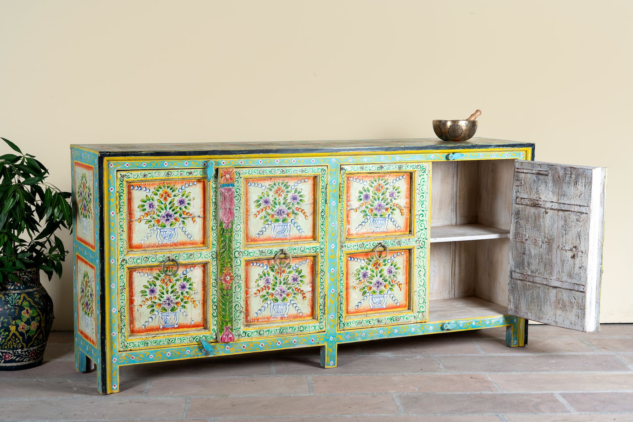 Side angle image with open door of a reclaimed wood sideboard with hand painted floral motifs and distressed finish; artisanal storage furniture for bohemian interiors, 170 × 40 × 104 cm.