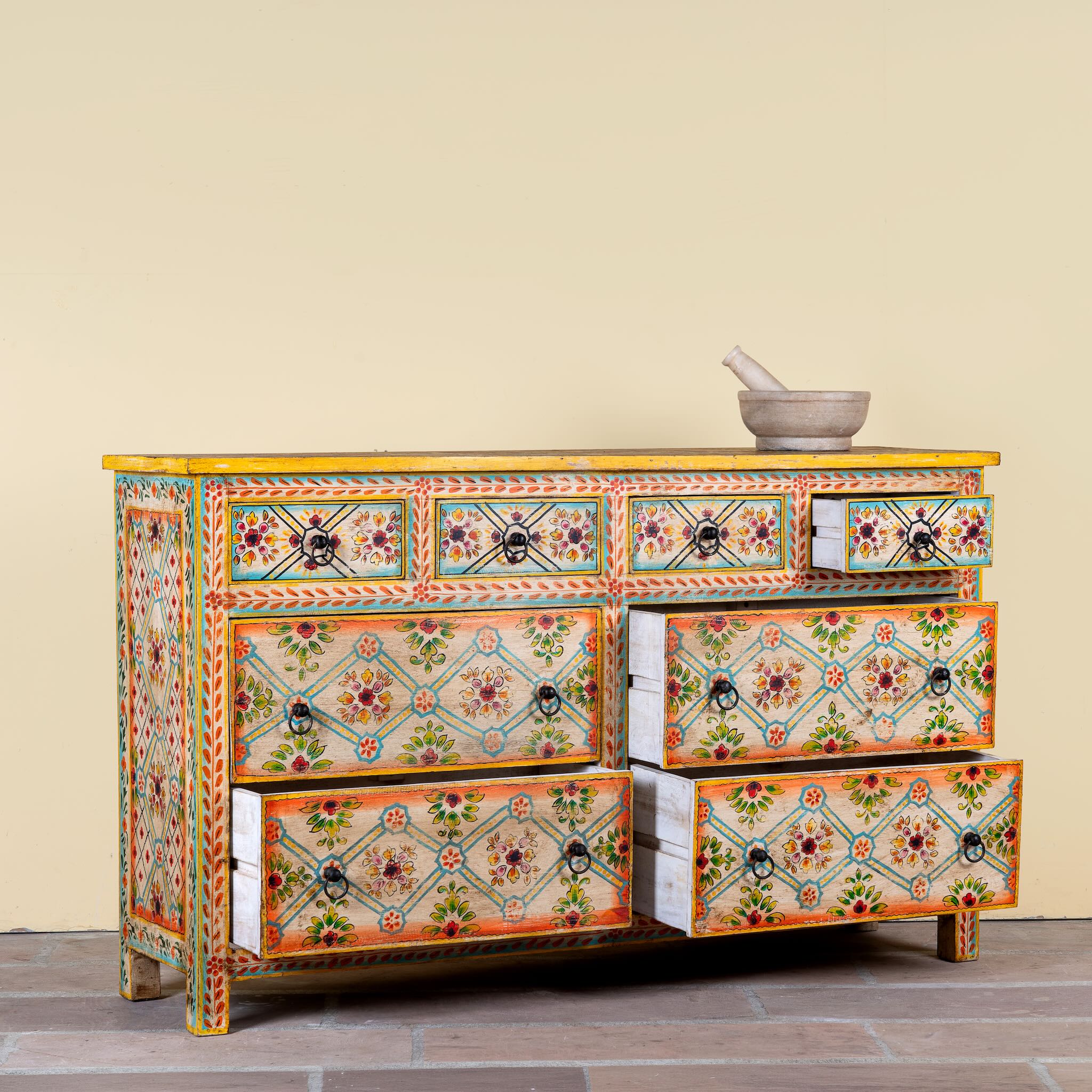 Side angle image with open drawers of a Ziya hand‑painted chest of 8 drawers made from reclaimed wood with floral motifs and iron handles—an artisan piece of painted wooden furniture.