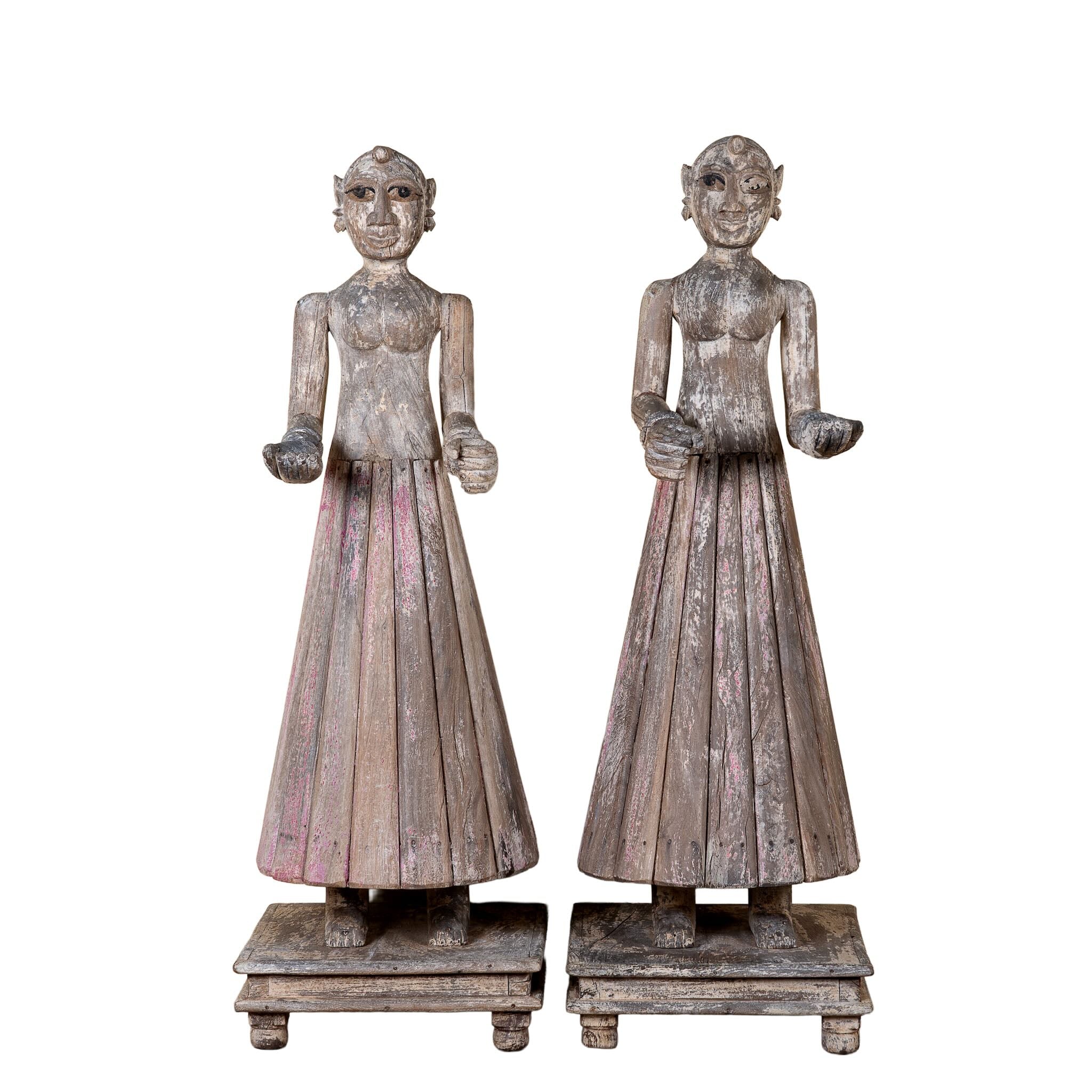 White background image of an antique Indian wooden temple guardian figure with weathered patina, styled beside a black-framed door in a modern living room.