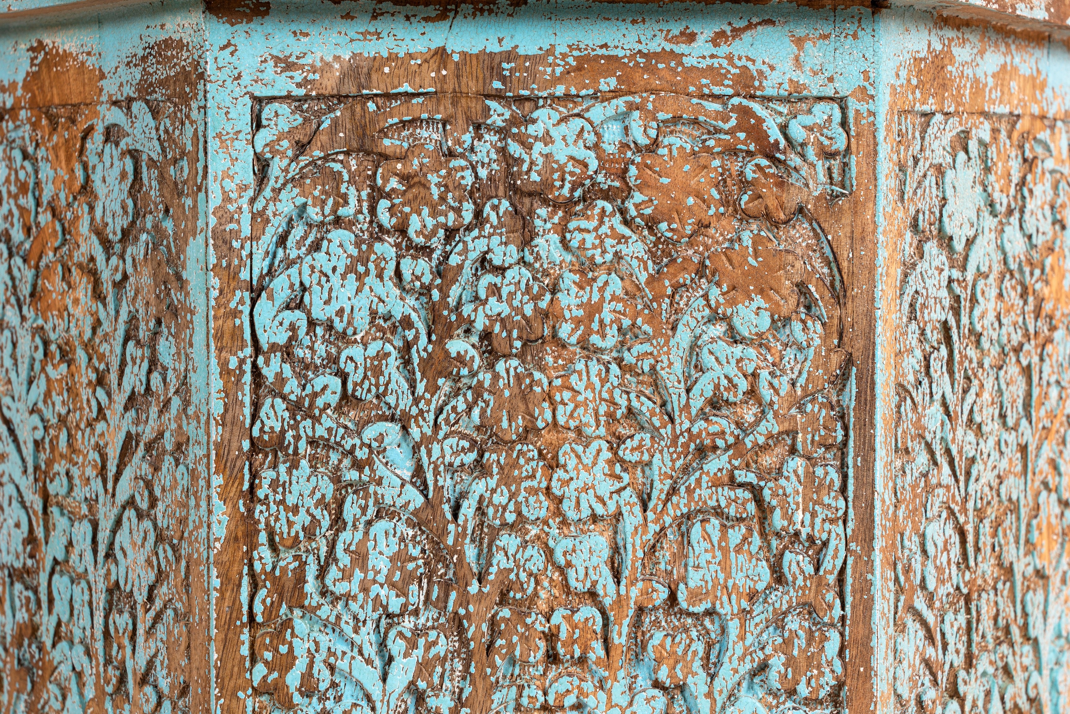 Close up image of a of a hand carved decorative side table with arched design next to a bed in a bedroom.