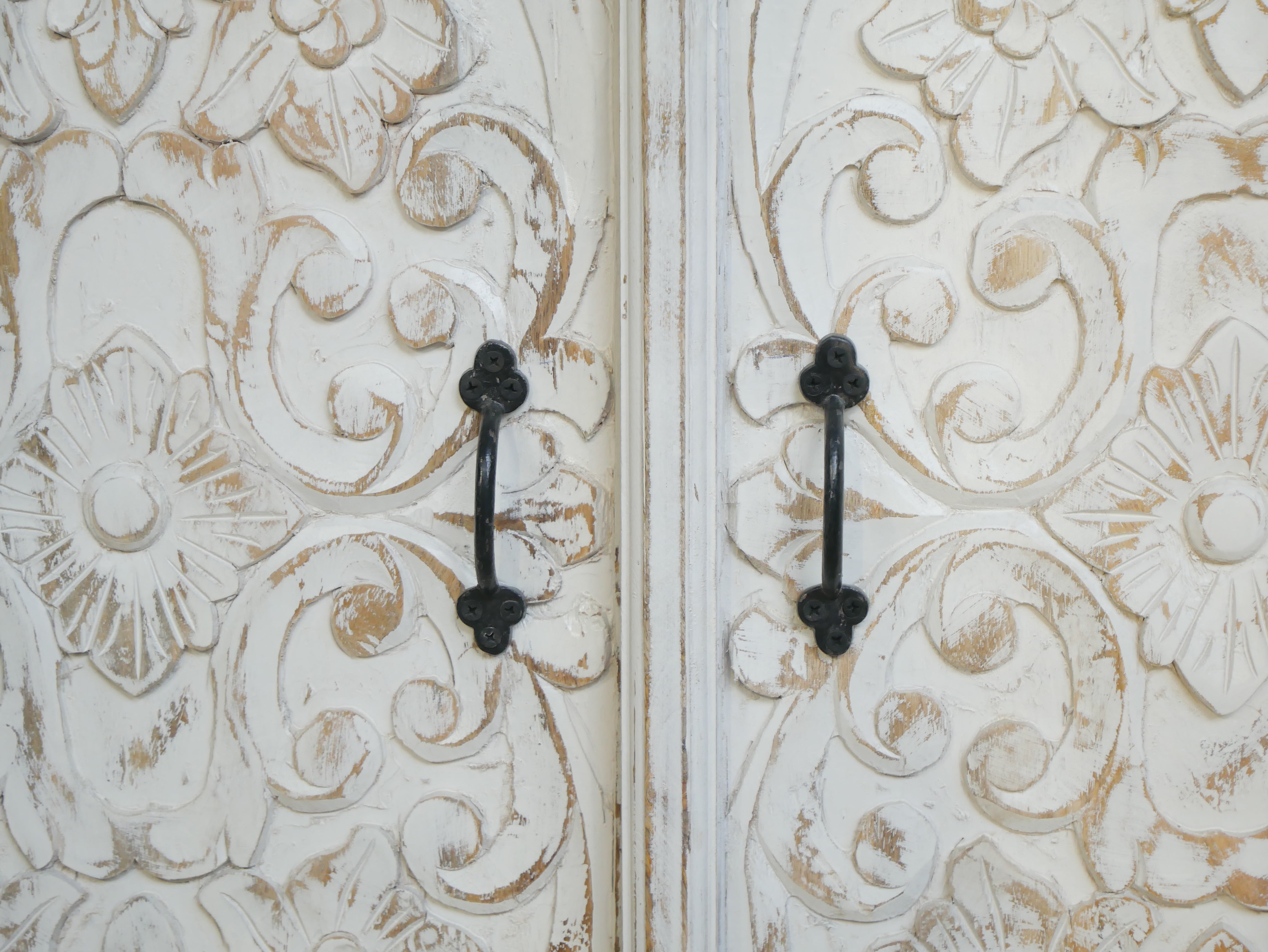 Close up image of a white washed wooden cabinet made from mango wood with hand-carved Indian floral patterns, rustic Mediterranean-style furniture, 90 × 97 × 40 cm.