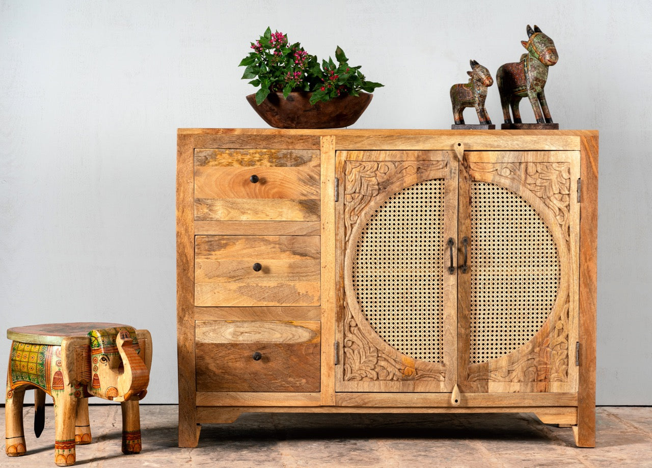 Image with a hand carved mango wood cabinet in natural finish with 3 drawers and 2 rattan doors.
