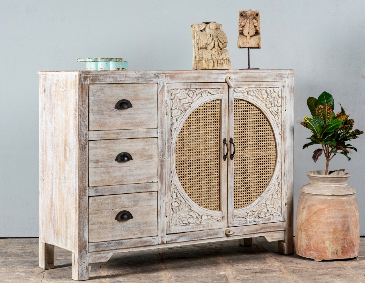 Side angle image of a handcrafted mango wood dresser with floral carvings and rattan cane inserts, bohemian interior and rattan furniture style, whitewashed finish, 120 × 40 × 92 cm.