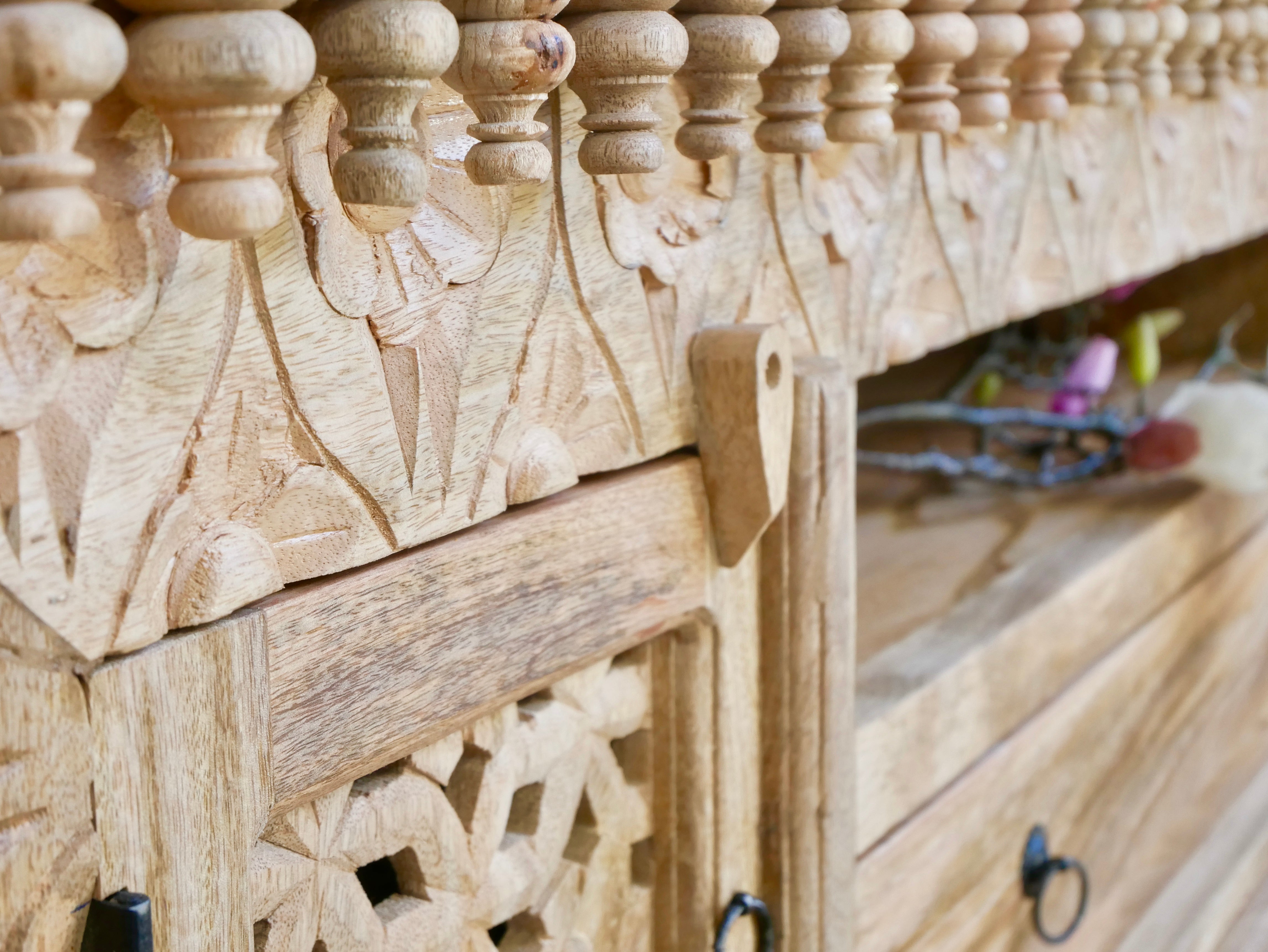 Close up image of a carved mango wood TV unit with hand-carved doors, one drawer, and open shelf, 150 × 60 × 40 cm.