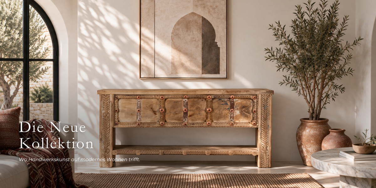 A carved wooden sideboard or console table with multiple drawers and decorative metal accents, shown in a styled interior room with sunlight, a framed arch artwork, potted plants, and German text overlay reading 'Die Neue Kollektion'.