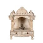 White background image of a decorative Indian altar made of mango wood, hand carved with 2 small drawers in a living room with a couch and coffee table.