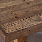 Close up image of a rectangular rustic coffee table constructed from reclaimed wood, featuring a thick plank-style top and wide block legs, all with a naturally weathered finish that highlights the wood’s grain and imperfections.
