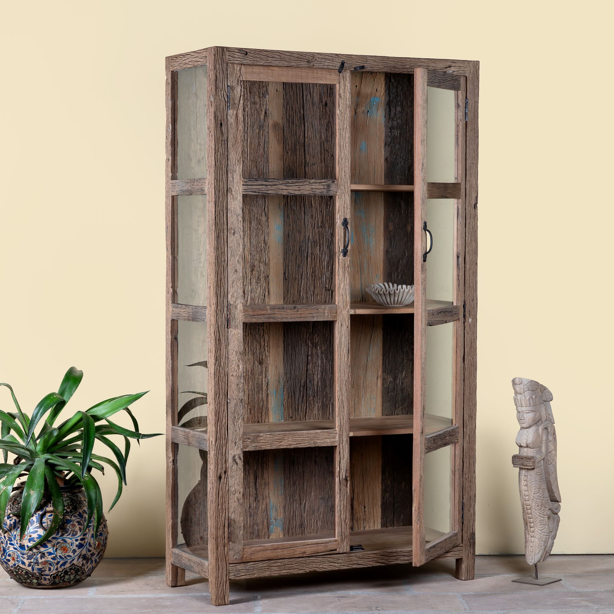 Side angle with open door of a driftwood display cabinet with 2 glass doors and 4 shelfs in rustic design.