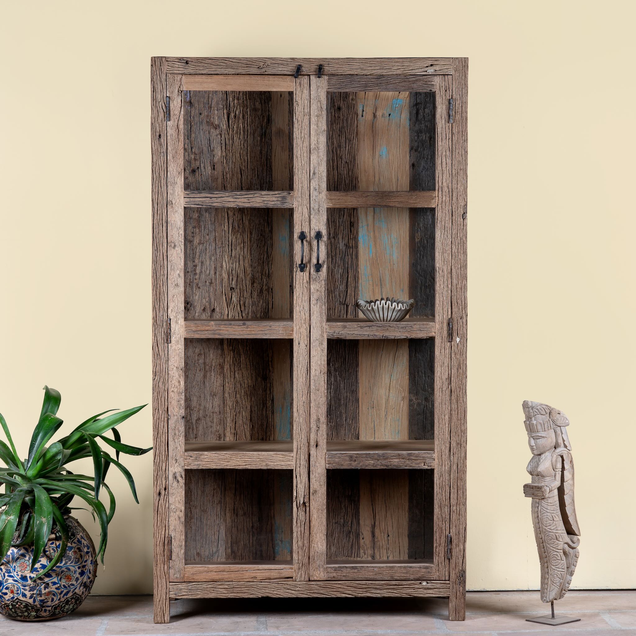 Lifestyle image of a driftwood display cabinet with 2 glass doors and 4 shelfs in rustic design.
