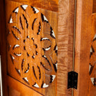 Side angle image of a foldable room partition made of mango wood, featuring four panels with symmetrical hand-carved circular floral medallions, finished in a rich natural wood tone and connected by black metal hinges for easy folding and adjustment.
