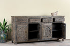 Side angle image with open doors of a hand-carved mango wood sideboard Aavya in a vintage dark finish, featuring four drawers and four carved cabinet doors with Indian-inspired motifs. A bold piece of vintage furniture and unique Indian craftsmanship.