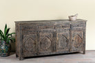 Side angle image of a hand-carved mango wood sideboard Aavya in a vintage dark finish, featuring four drawers and four carved cabinet doors with Indian-inspired motifs. A bold piece of vintage furniture and unique Indian craftsmanship.