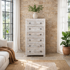 Lifestyle image of a hand carved white washed mango wood chest of 6 drawers in mediterranean design with iron 
handles.