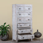 Side angle image of a hand carved white washed mango wood chest of 6 drawers in mediterranean design with iron 
handles.