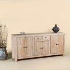 Side angle image of a sandblasted wooden sideboard with three compartments and two small drawers, Ibiza style living room furniture in light natural finish, 200×40×90 cm.