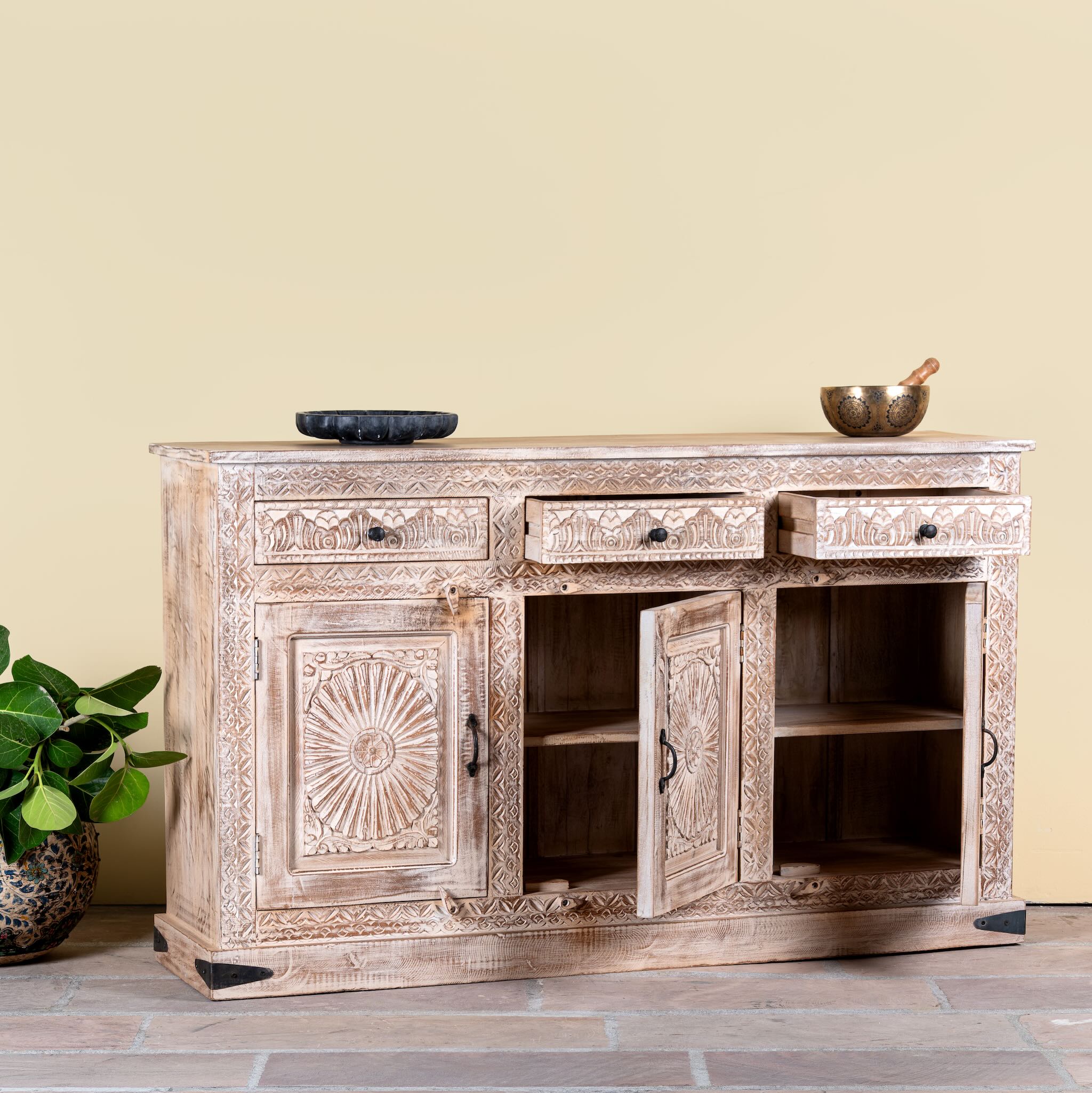 Side angle image with open doors of a Abhiraj hand carved mango wood sideboard with distressed cream finish, three drawers and three doors, 150cm