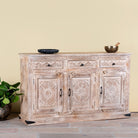 Side angle image of a Abhiraj hand carved mango wood sideboard with distressed cream finish, three drawers and three doors, 150cm