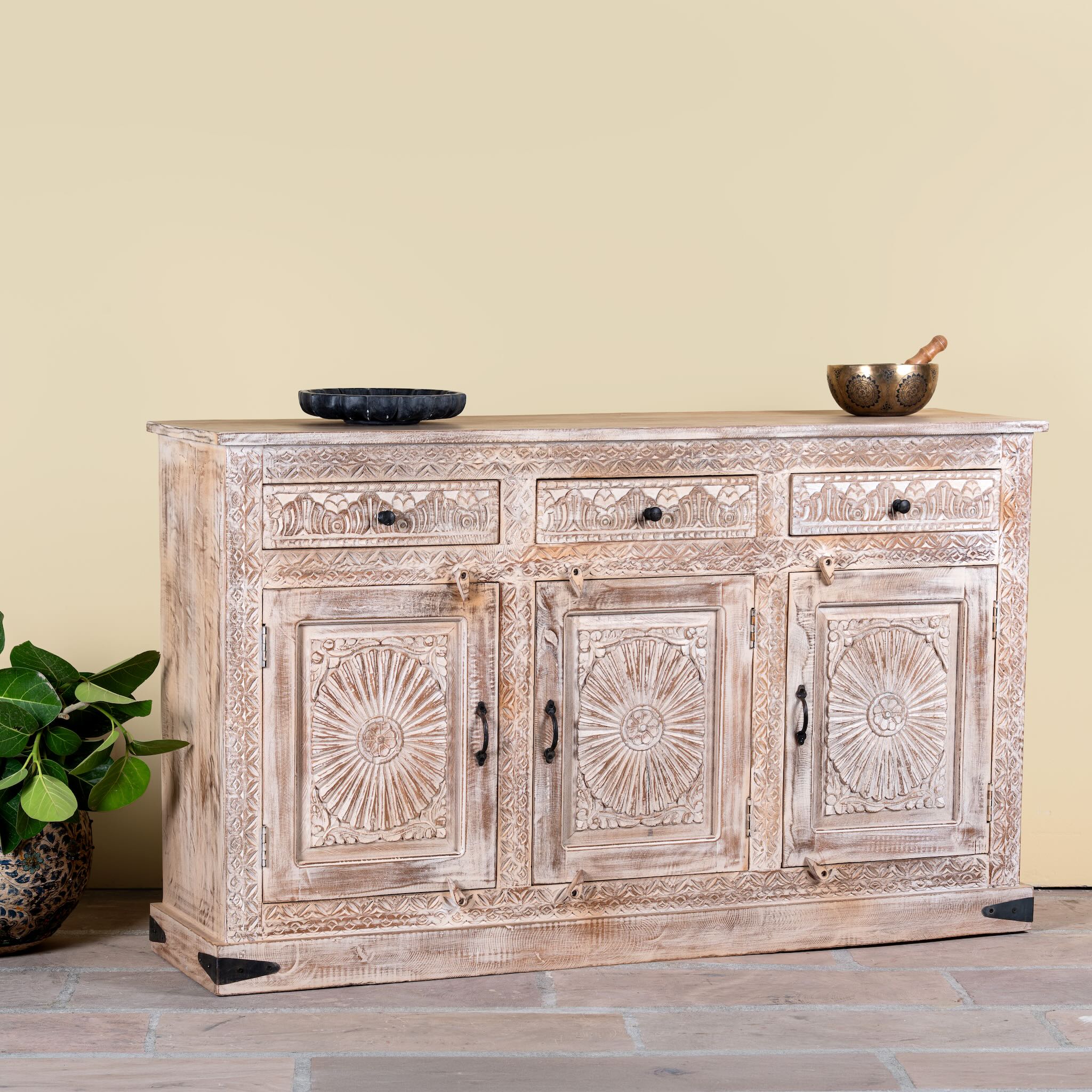 Side angle image of a Abhiraj hand carved mango wood sideboard with distressed cream finish, three drawers and three doors, 150cm