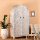 Side angle image of an arched wooden wardrobe made of mango wood with hand-carved floral details; hand carved wooden furniture in Ibiza style, 190 × 100 × 40 cm.