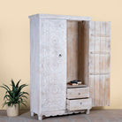 Side angle image with open door of a hand carved white washed mango wood wardrobe in vintage design.