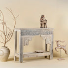 Side view image of a handcrafted reclaimed teak wood console table with sandblasted finish, carved floral detailing, vintage corbels, and lower shelf; perfect for styling with vintage home accessories, 133 × 62 × 90 cm.