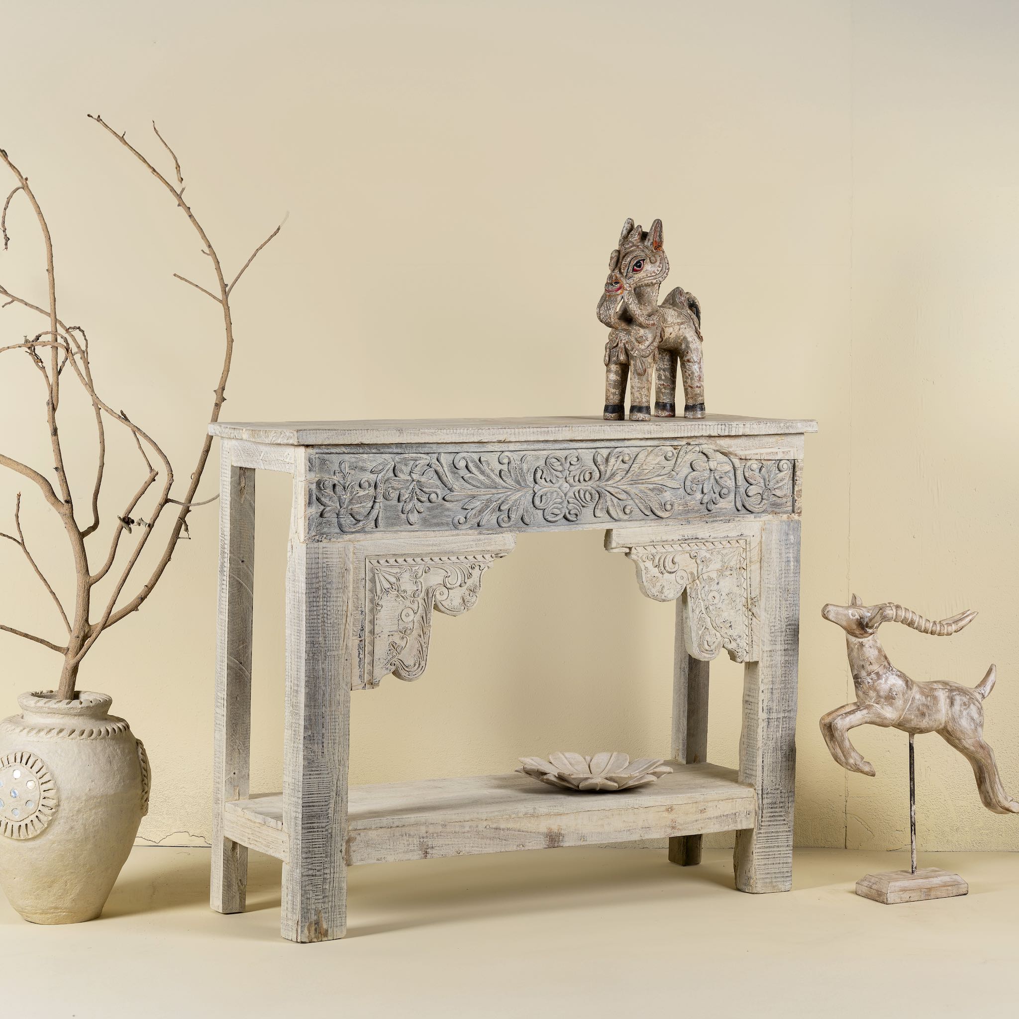 Side view image of a handcrafted reclaimed teak wood console table with sandblasted finish, carved floral detailing, vintage corbels, and lower shelf; perfect for styling with vintage home accessories, 133 × 62 × 90 cm.