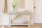 Lifestyle imagination of a handcrafted reclaimed teak wood console table with sandblasted finish, carved floral detailing, vintage corbels, and lower shelf; perfect for styling with vintage home accessories, 133 × 62 × 90 cm.